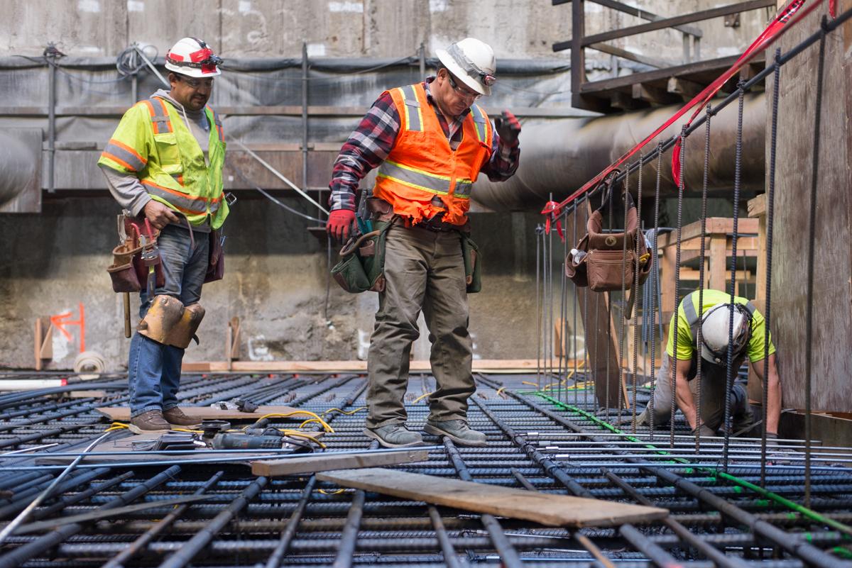 Construction workers install rebar reinforcement on a concrete floor slab at an underground transit station.