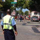 Traffic control officer in safety vest directing pedestrians and vehicles on city street during construction.