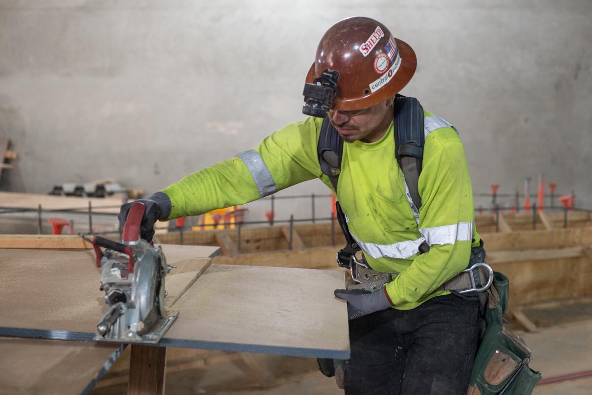 Worker in safety gear cutting plywood with a circular saw on a construction site.