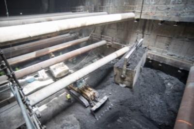Interior view of transit station excavation showing concrete support beams and construction equipment in underground work area.