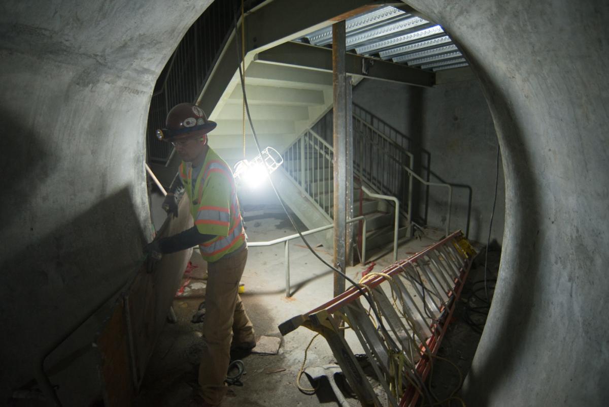 Worker in safety gear inspecting concrete tunnel interior with metal railings and corrugated flooring.