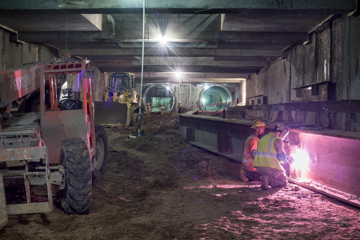 Workers weld steel brackets inside Yerba Buena station tunnel during construction.