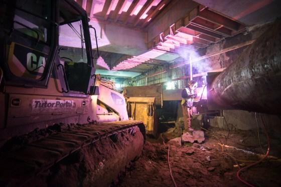 Construction equipment and pink lighting inside underground transit station work area at night.