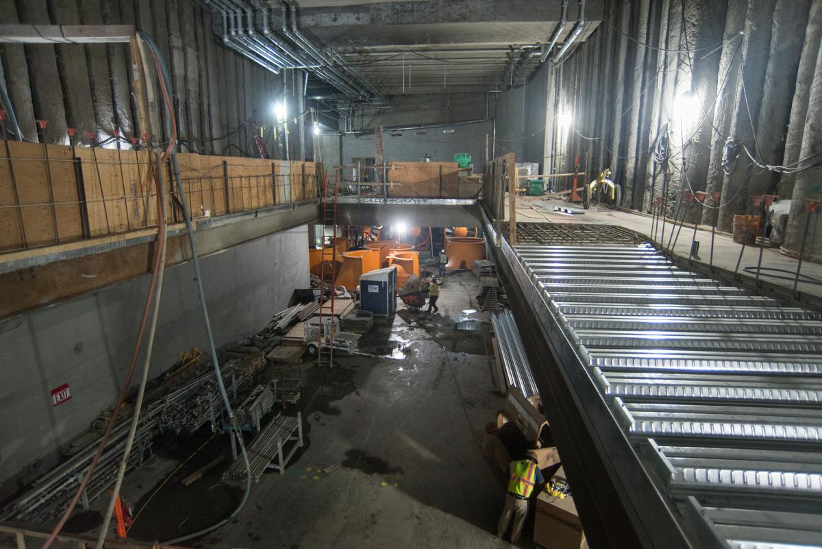 Workers construct new floor slab sections in underground transit station concourse with metal framework and equipment.