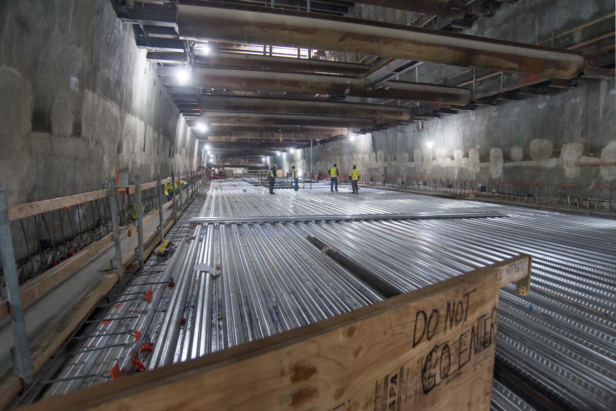 Construction workers install corrugated steel decking inside underground transit station box.