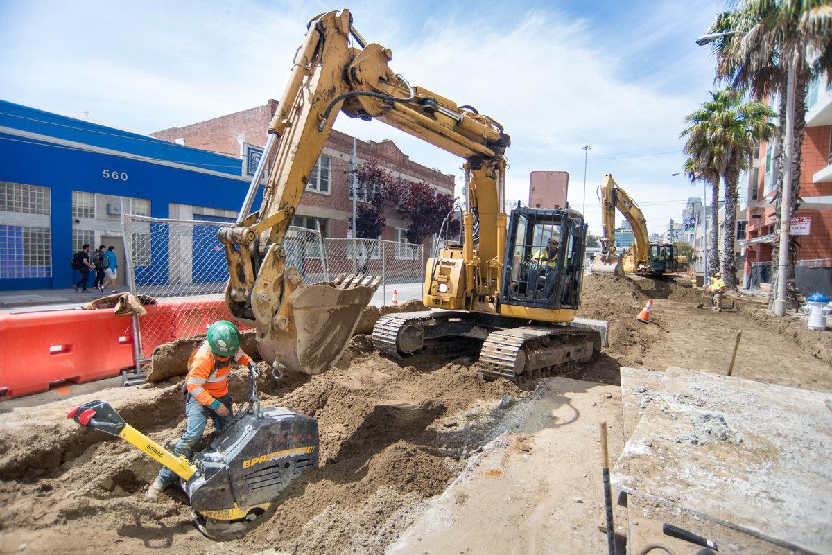 Construction crew operates excavator and compacting equipment during Central Subway Project work at 4th and Freelon.