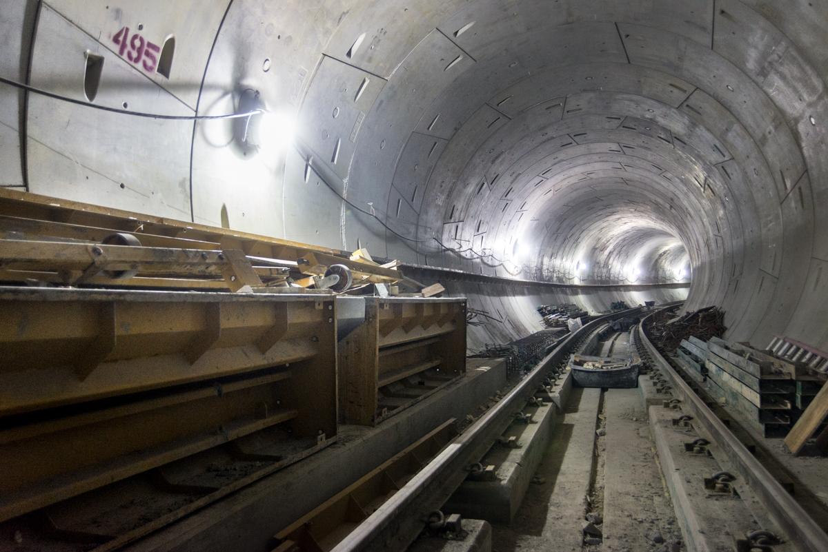 Northbound tunnel under construction with track installation and concrete walkways visible extending toward the S-curve.