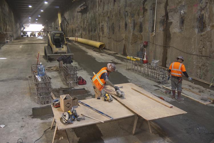Workers in orange vests assemble tunnel boring machine components in an underground construction site.