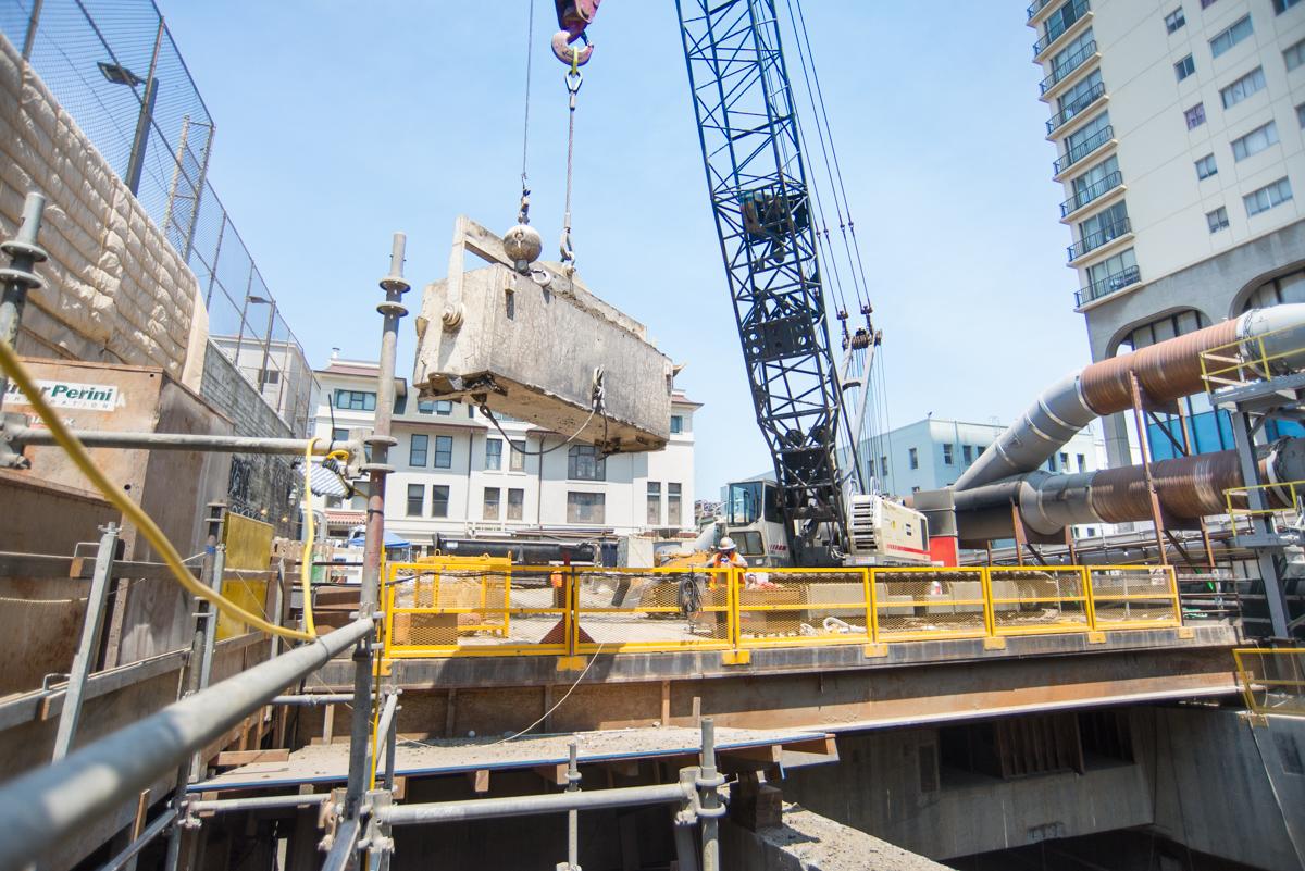 Construction crane lifting excavated material from transit station headhouse into bucket on platform