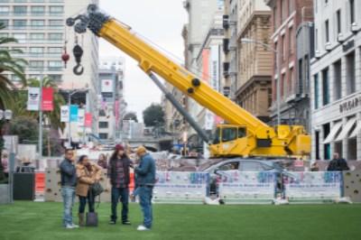 Yellow construction crane on city street with Winter Walk event setup and pedestrians below