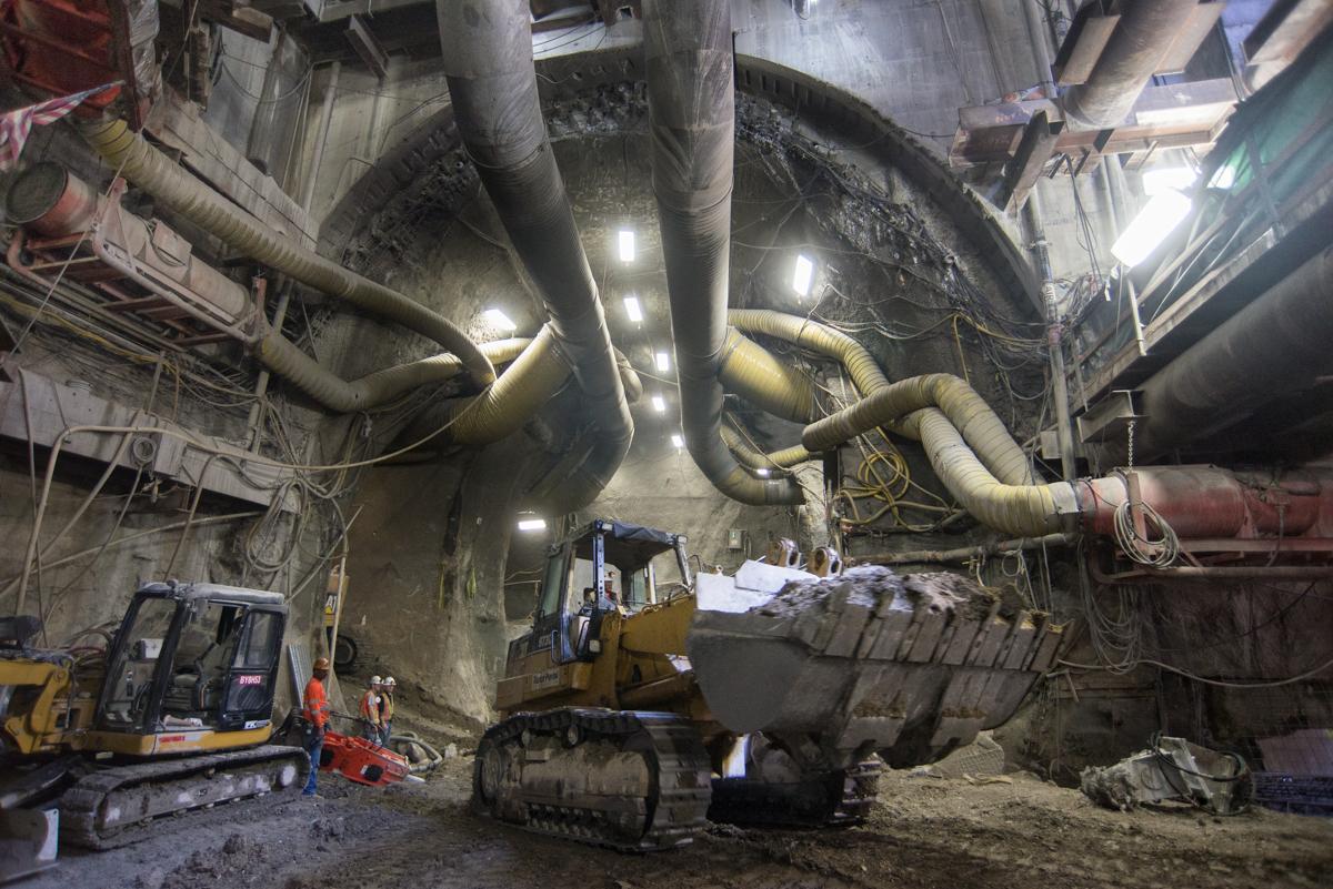 Bulldozer with full bucket inside underground tunnel with large pipes and LED lighting