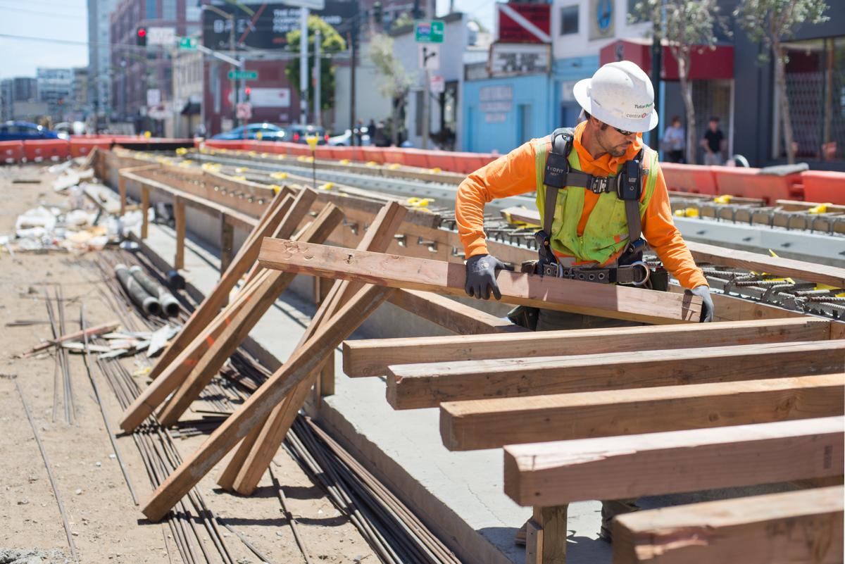 Construction worker installing wooden beams for station platform formwork on urban transit project.
