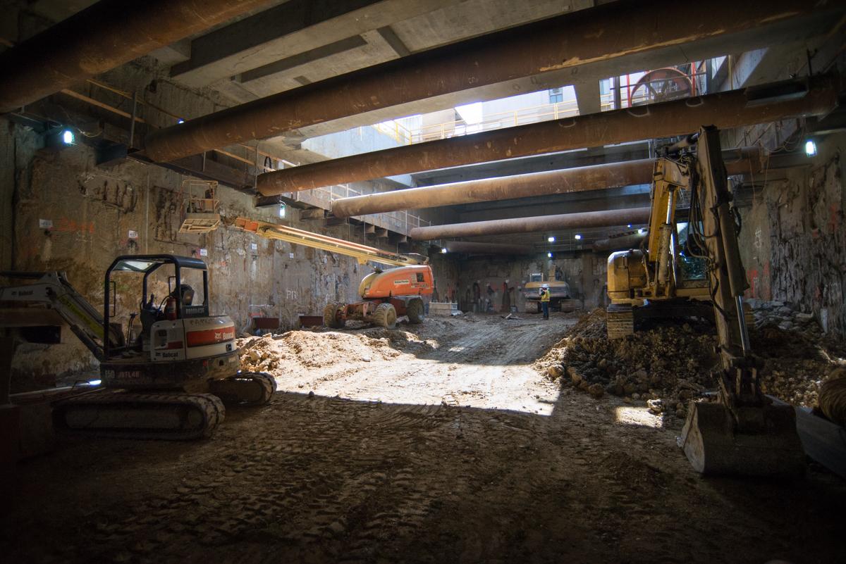 Construction equipment and excavation work inside Chinatown station headhouse with temporary steel supports.