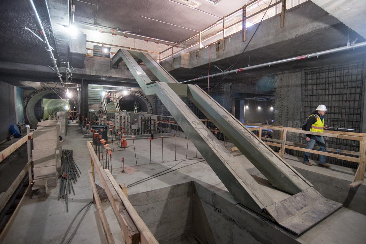 Construction of concrete staircase and escalator in underground transit station with worker in safety gear.