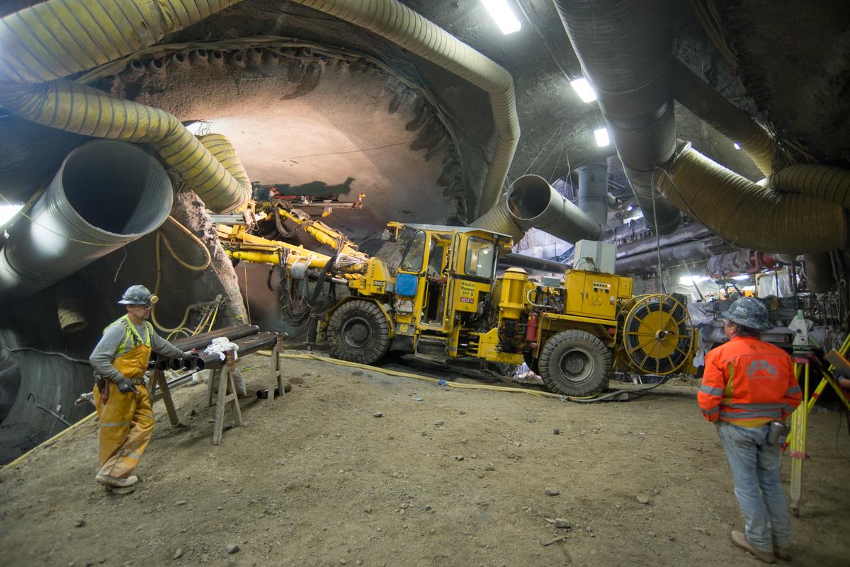 Workers operate yellow drilling equipment inside an underground tunnel during Central Subway construction.