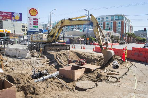 Excavator digs at 4th and Bryant streets for water and sewer line installation during Central Subway construction.
