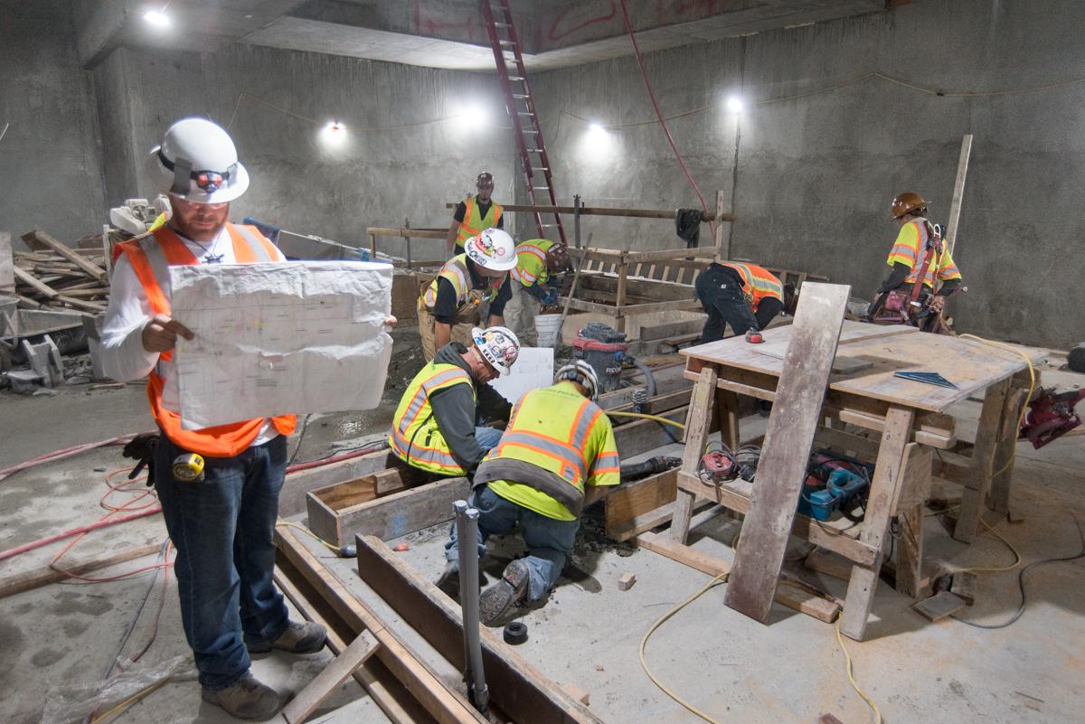 Construction workers in safety gear prepare concrete forms for interior wall footings inside Yerba Buena/Moscone Station.