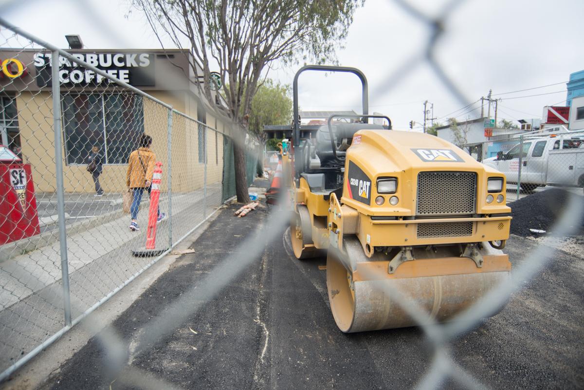 Yellow CAT road roller compacting asphalt on street next to Starbucks behind chain-link fence.