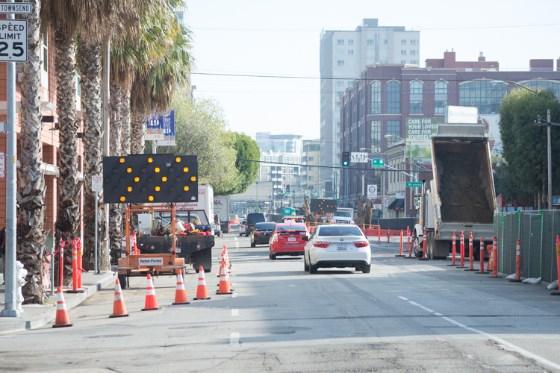 Urban street with construction barriers, orange cones, and detour signage blocking a lane in downtown San Francisco.