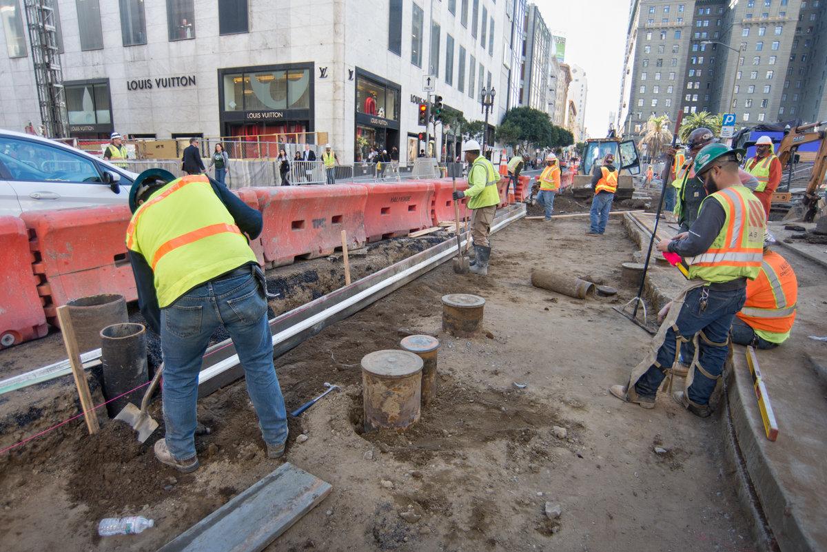 Construction workers in safety vests excavate underground utilities on a city street near Union Square.