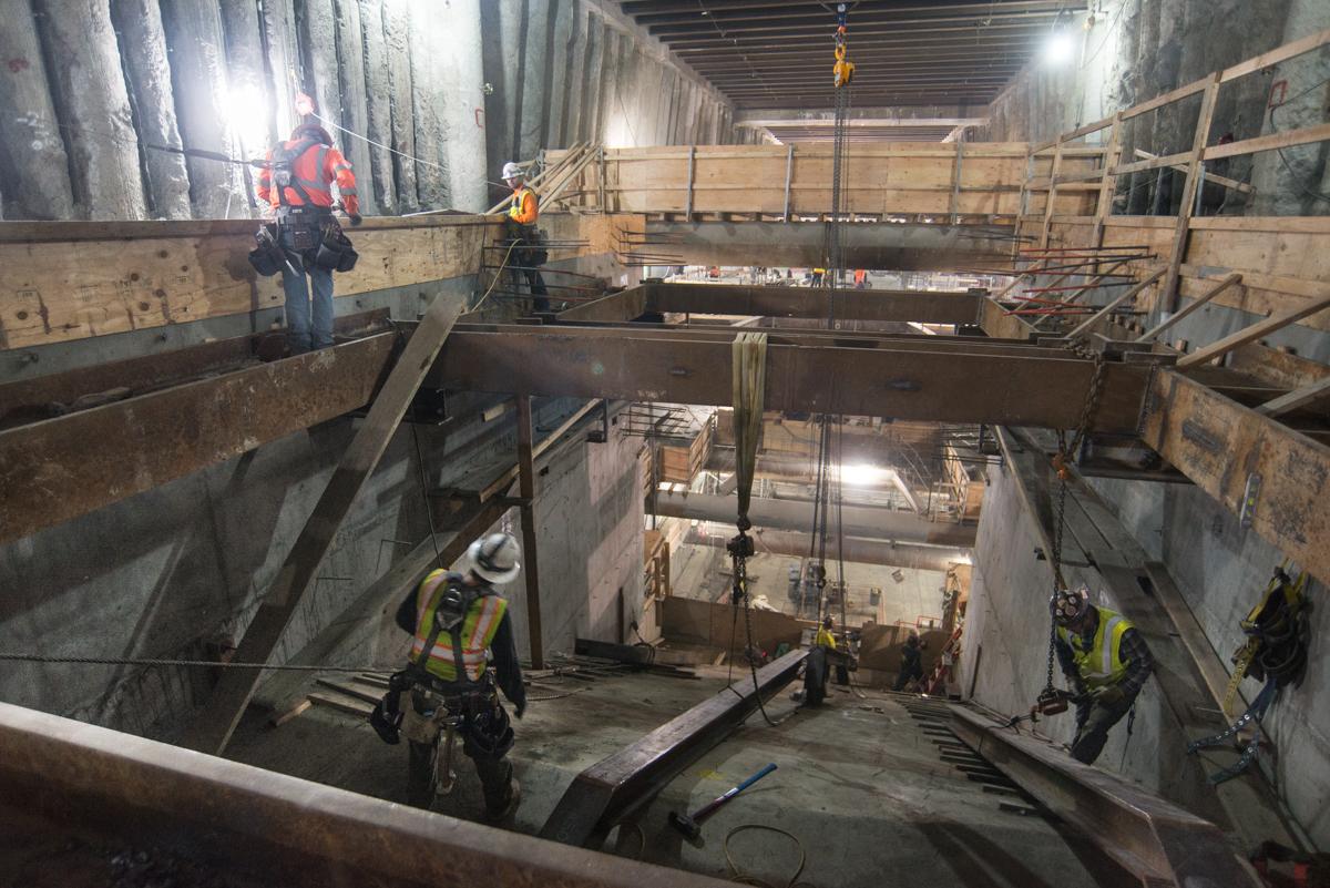 Construction workers in safety gear assemble steel framing and concrete forms in an underground transit tunnel.