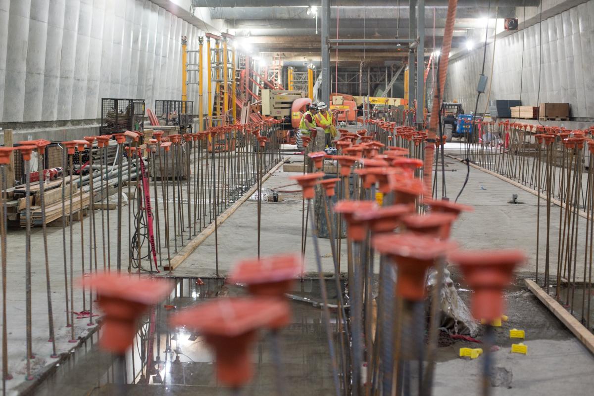 Construction site with metal barriers, rebar, and wet concrete floor in industrial warehouse setting.