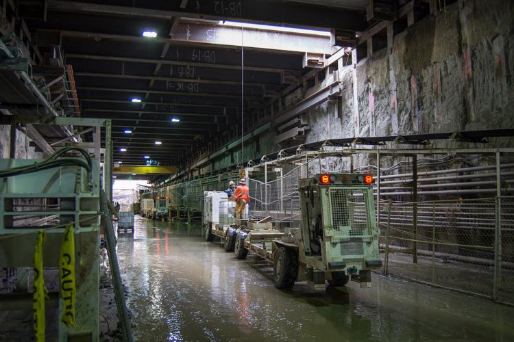 Industrial warehouse with green machinery and wet floor, fluorescent lighting overhead.