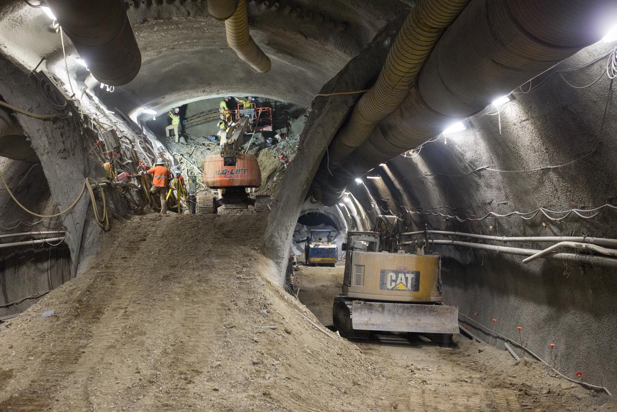 Underground tunnel construction with CAT equipment, workers, and excavated soil beneath concrete ceiling and pipes.