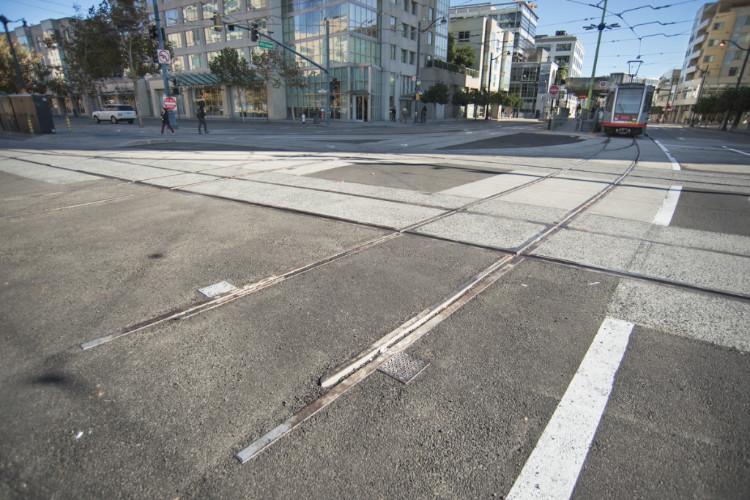 New streetcar tracks crossing an urban intersection with buildings and a tram visible in the background.
