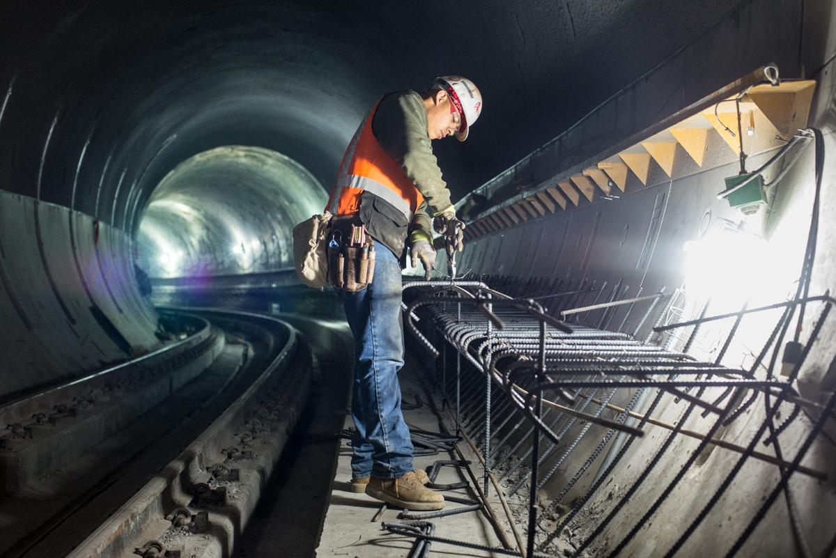 Worker securing rebar with wire inside a subway tunnel under construction.