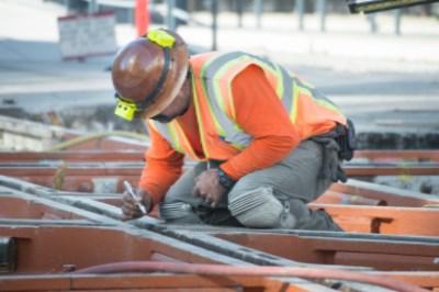 Construction worker in safety gear marking junction where N Judah and T line tracks cross on 4th Street.