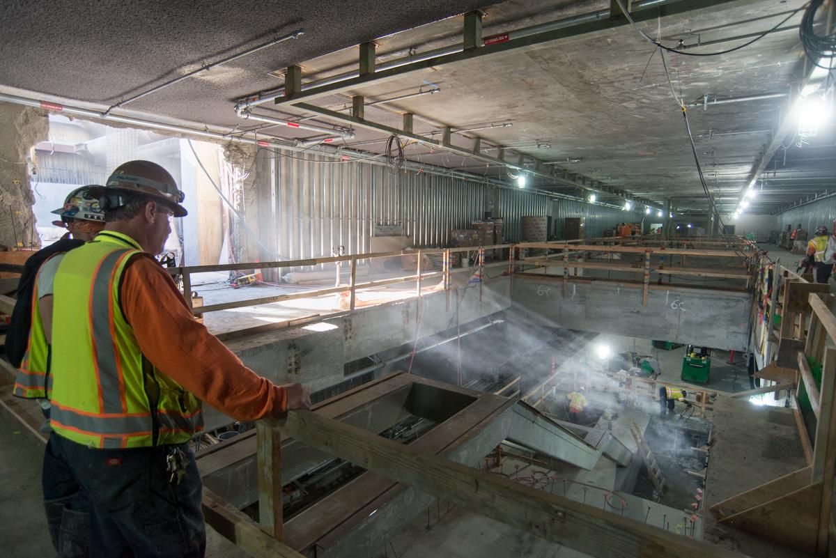 Construction worker in safety gear overlooking underground transit station excavation with concrete foundation work in progress.