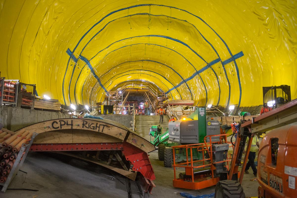 # Alt Text:</p>
<p>Interior of yellow tunnel under construction with equipment, machinery, and workers visible along the floor.