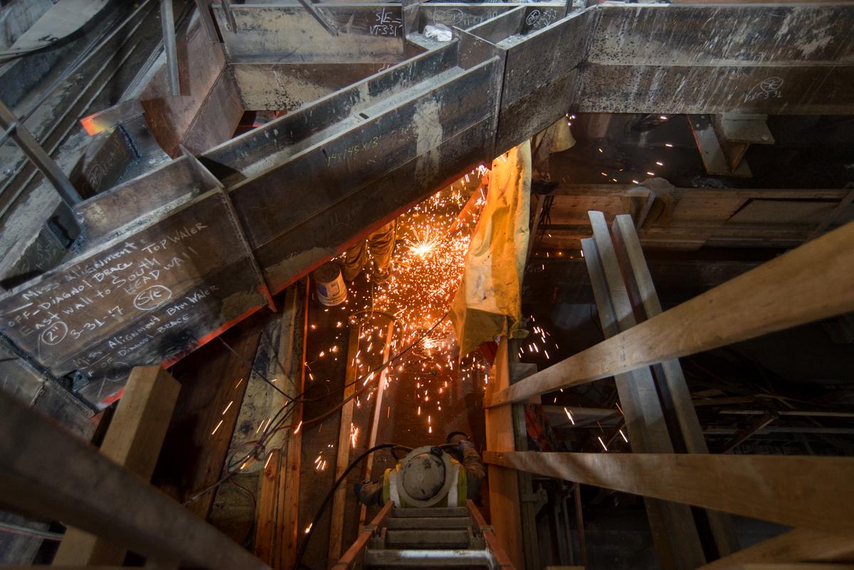 Welder creating sparks while working on temporary bracing at Union Square/Market Street Station construction site.