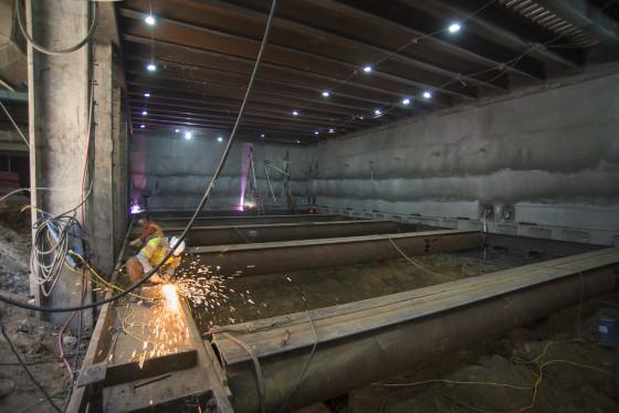 Worker using angle grinder on reinforcing beam inside transit tunnel under construction.