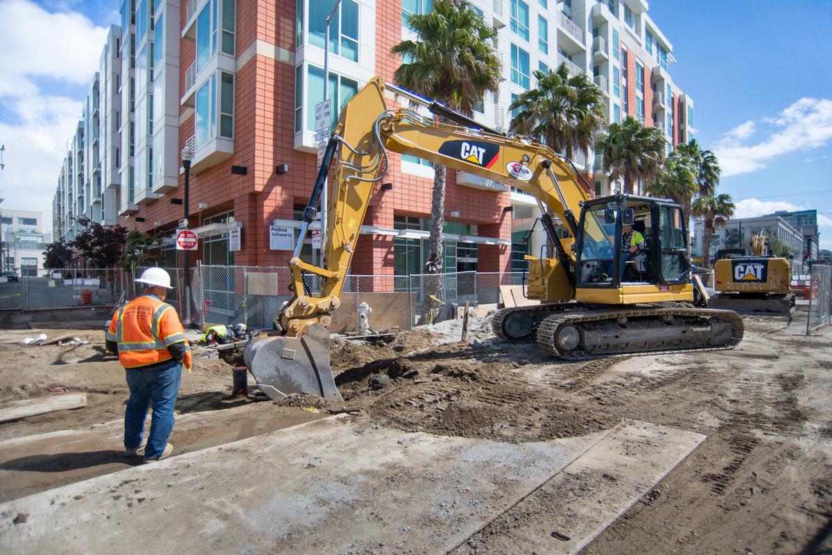 Construction crew operating yellow CAT excavator while backfilling utility trenches at 4th and Welsh Street.