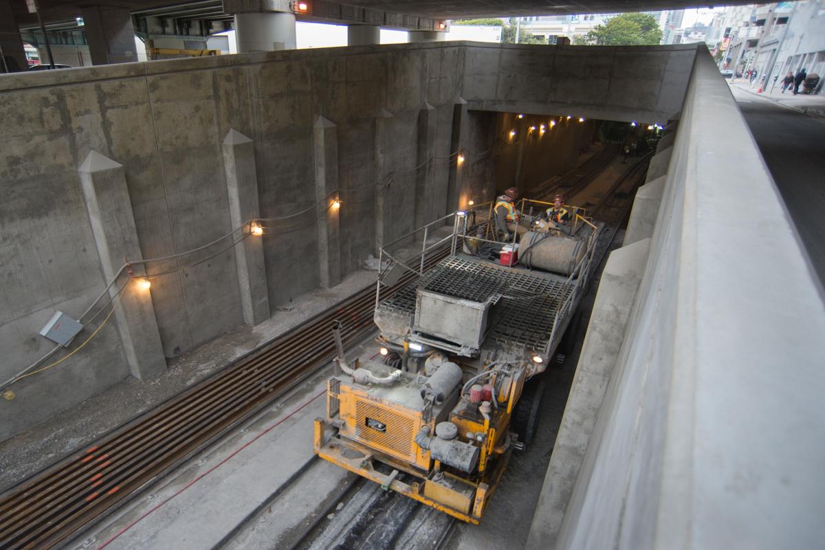 Yellow concrete pump truck entering tunnel portal on underground transit track with concrete support columns visible.