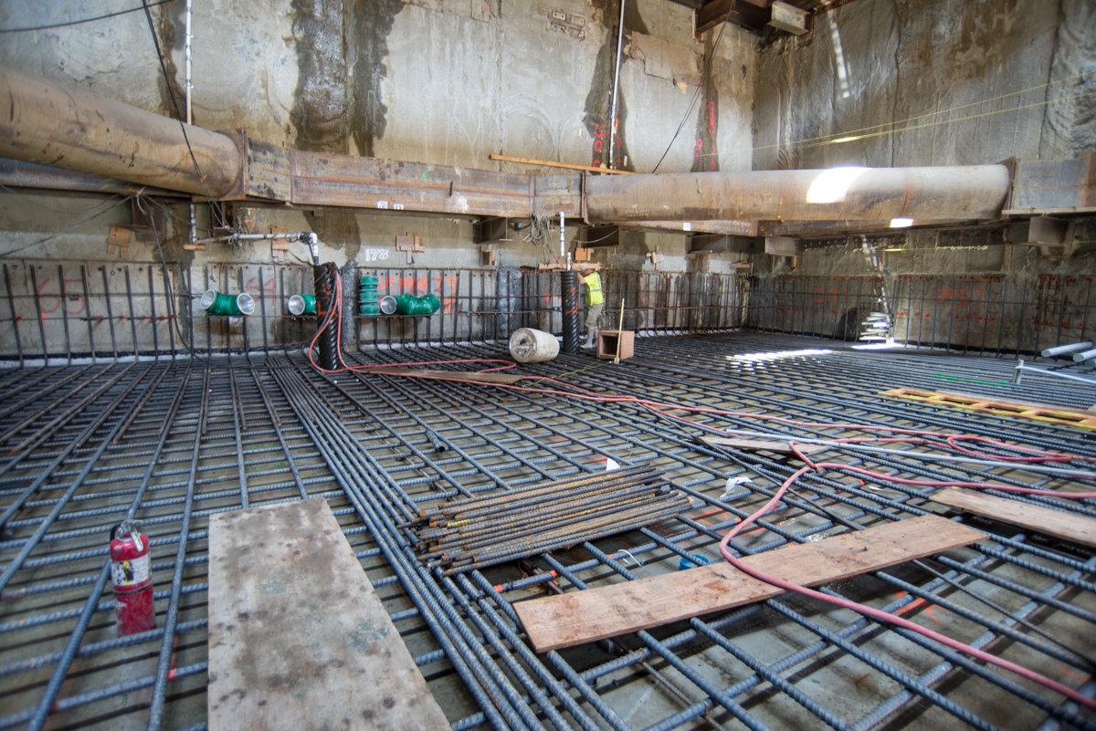 Construction site with steel rebar grid and temporary bracing installed at station platform level