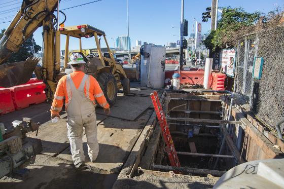 Worker in orange safety vest stands in excavation pit at 4th and Bryant streets during AT&T vault installation.
