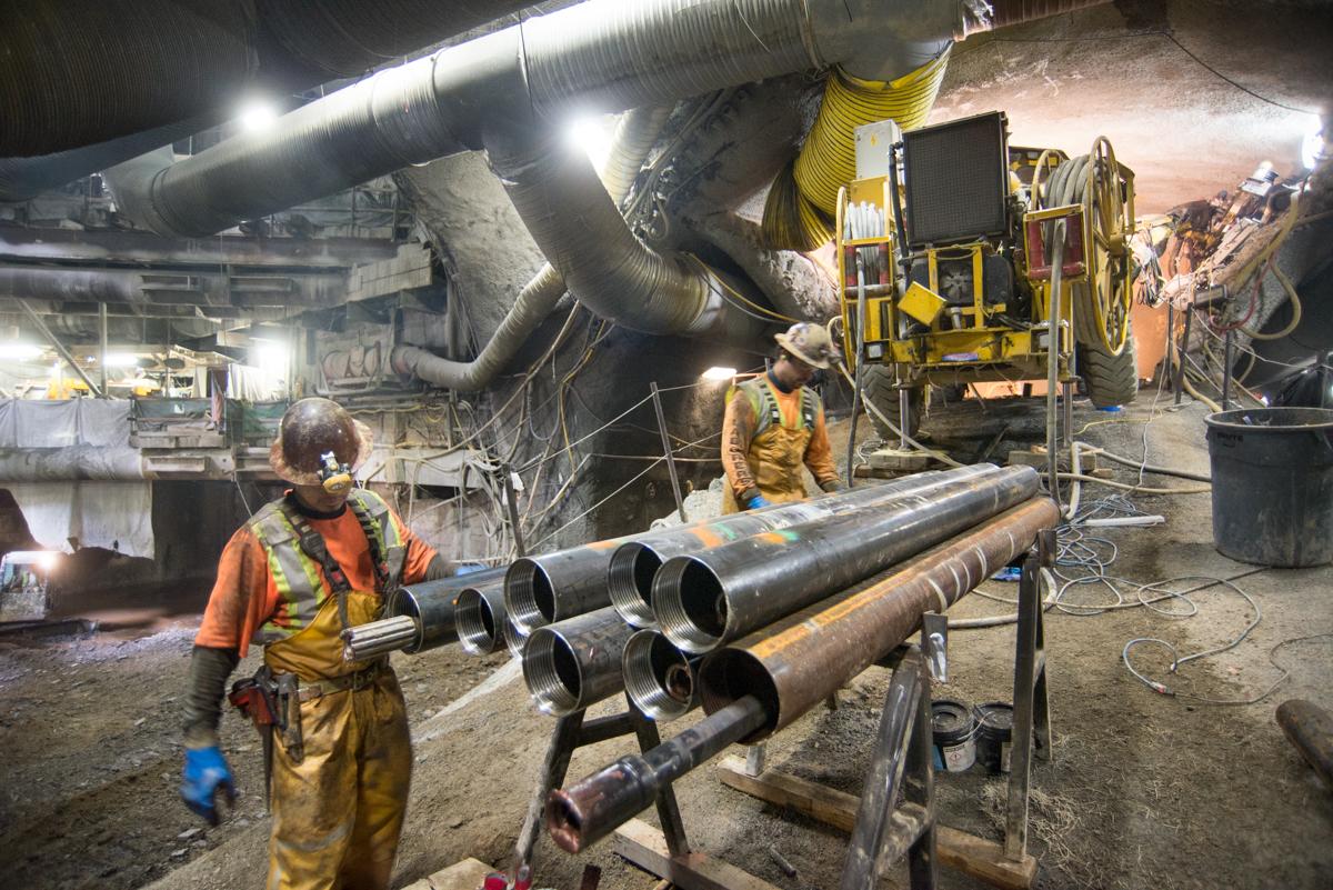 Workers in hard hats operate drilling equipment inside an underground transit tunnel construction site.