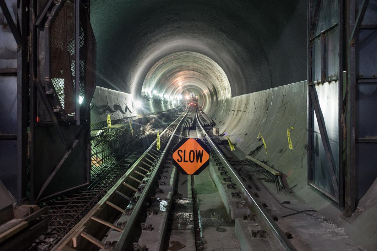Southbound tunnel with railroad tracks, SLOW sign, and utility vehicle approaching through circular concrete tunnel with lighting.