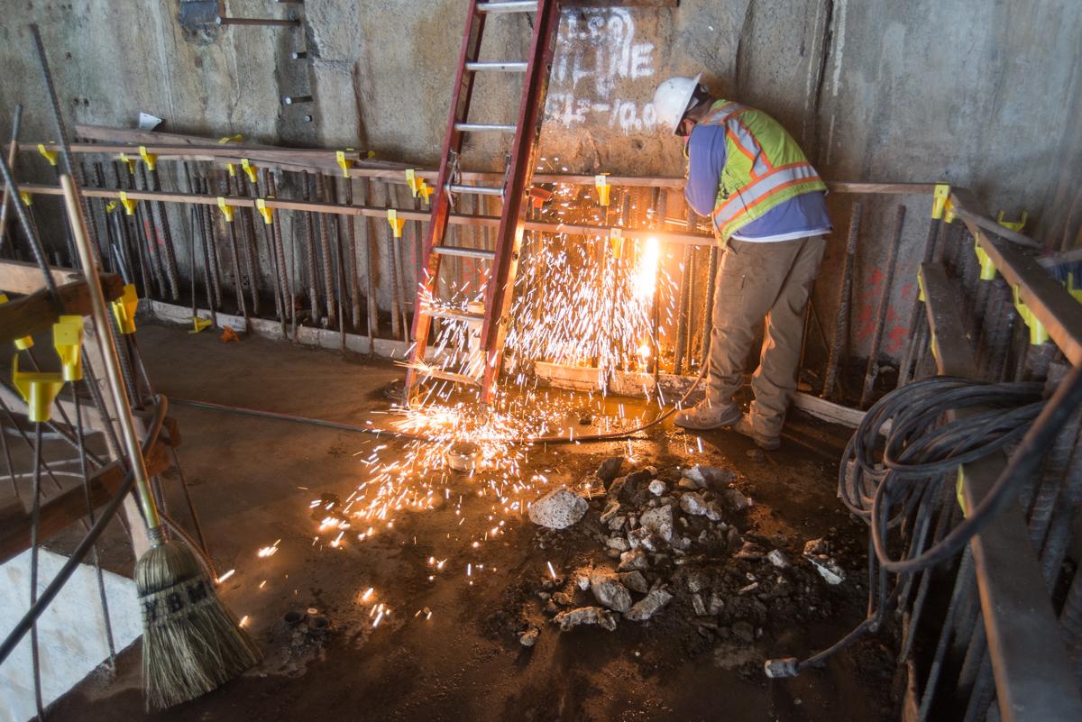 Worker in safety vest cutting steel rebar with sparks flying at construction site on 4th Street.