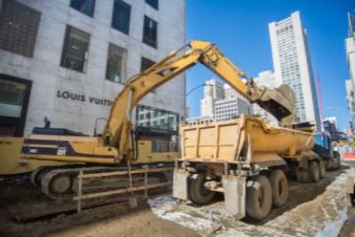 Yellow excavator loads soil into dump truck at Union Square construction site on Geary Street.