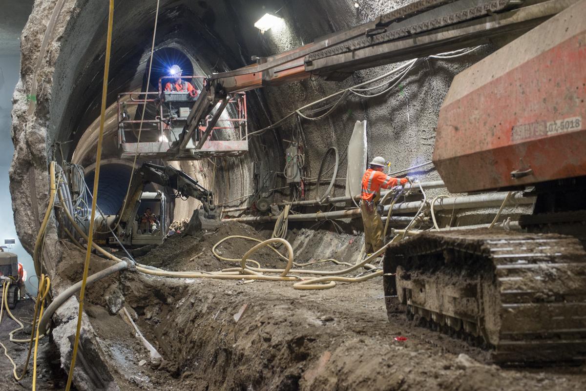 Workers operate equipment inside tunnel cavern during underground excavation and spoil removal.