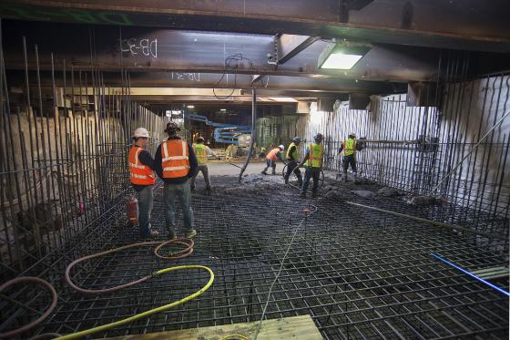 Construction workers in safety vests pouring concrete over rebar framework on 4th Street subway portal ramp.