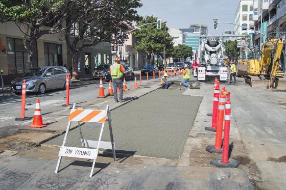 Workers pour concrete on 4th Street roadway with traffic cones and equipment visible.