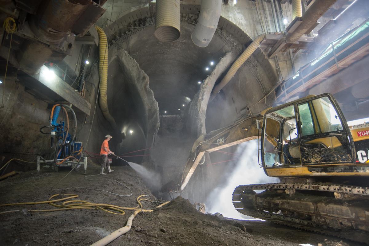 Worker sprays water on jackhammer removing slurry wall at Chinatown Station tunnel construction site.