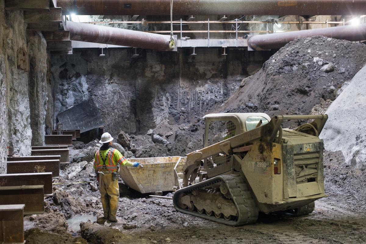 Construction worker directing Bobcat skid-steer loader during excavation in underground transit station cavern.