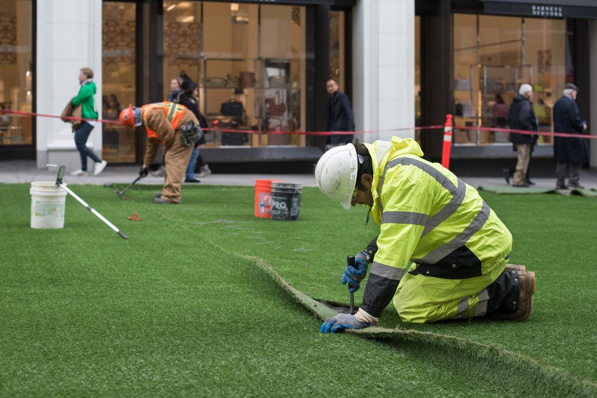 Worker in safety gear installing artificial turf for Central Subway project at downtown San Francisco location.