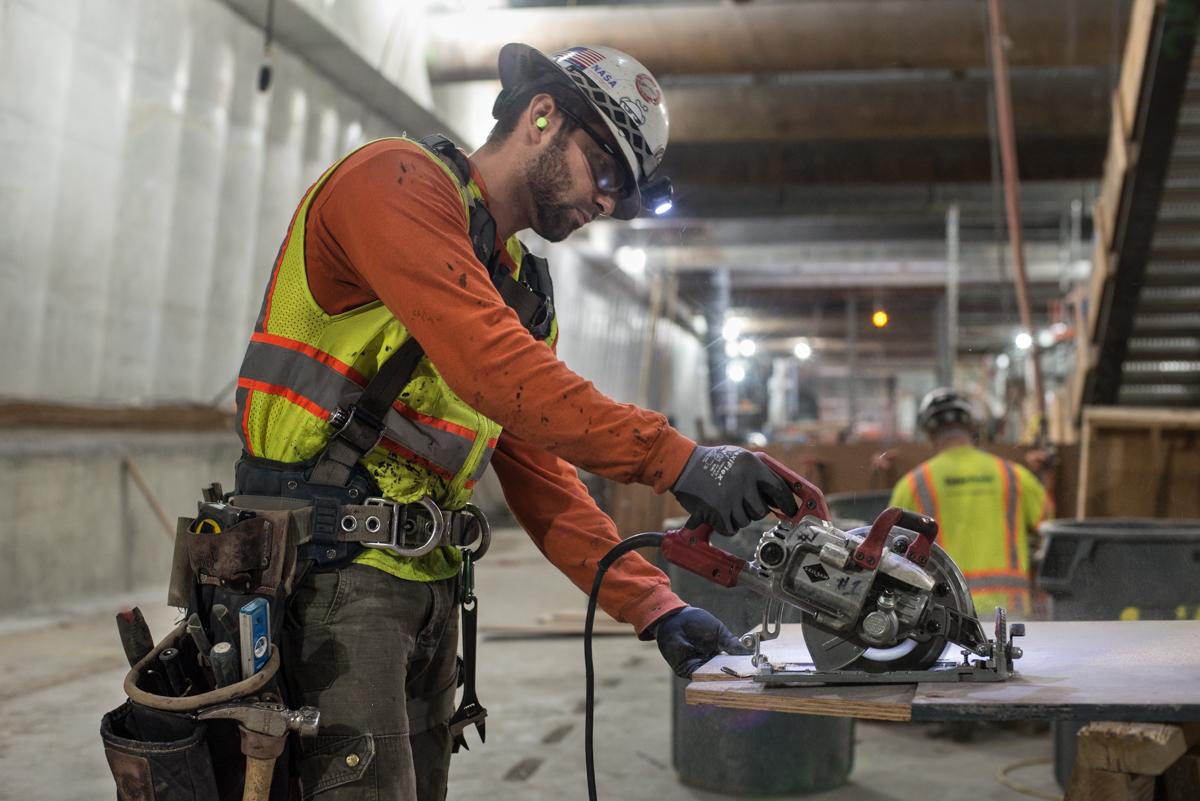 Worker in safety gear cutting plywood with a circular saw for concrete formwork on underground transit construction project.